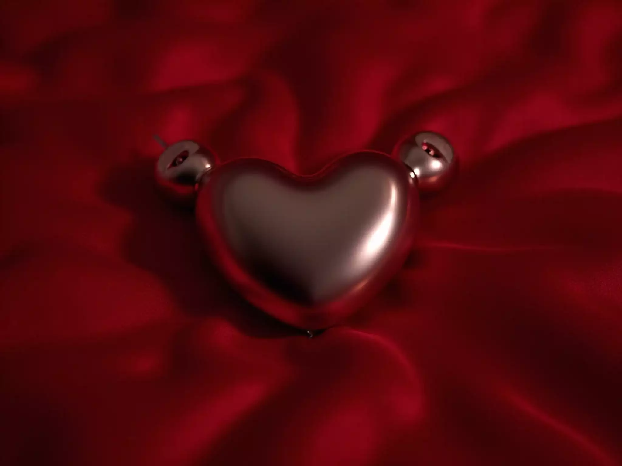 Electro anal plug with heart-shaped base and remote on red satin bedspread